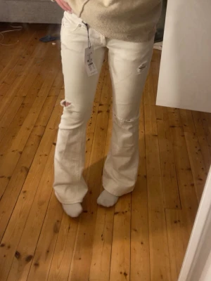 Vita bootcut jeans med slitningar - Säljer ett par vita bootcut jeans med slitningar. Det är i modellen tall. Inte alls använda mycket, ca 5 gånger 
