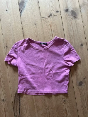 Ljuslila croppad topp från Zara - En enkel och snygg ljuslila croppad topp från Zara. T-shirten har rund halsringning och korta ärmar. Tillverkad i mjuk bomull som känns skön mot huden. Perfekt att matcha med höga jeans eller kjol.
