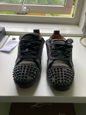 Svarta sneakers med nitar - Säljer ett par svarta sneakers med coola nitar på ovansidan. Skorna har lågt skaft och snörning framtill. Insidan är fodrad i beige och utsidan är i mockaliknande material. Perfekta för dig som vill sticka ut med din stil.