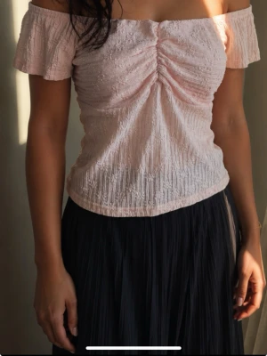 Ljusrosa off shoulder topp strl M  - Söt aprikos färgad off shoulder topp med korta ärmar och rynkdetalj framtill. Tillverkad i ett tunt, krinklat tyg som ger en avslappnad och trendig look. Perfekt att matcha med kjol eller jeans för en fräsch stil. Då inte rätt färg finns att fylla i så är den mer lite ljusare aprikos än rosa se bilder 