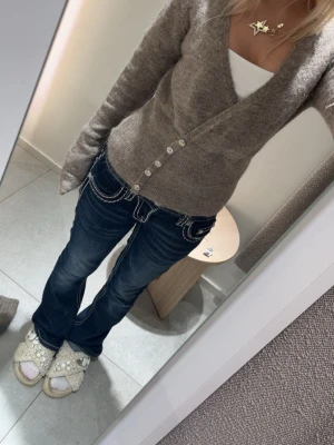 Beige omlottopp med knappar från Gina tricot  - Säljer en beige omlottopp med långa ärmar och dekorativa knappar framtill. Toppen är croppad och har en mjuk, stickad känsla som passar perfekt till jeans eller kjol. Enkel och stilren design som är lätt att matcha. Är i storlek xs och är ifrån Gina tricot. Har bara använts två gånger 