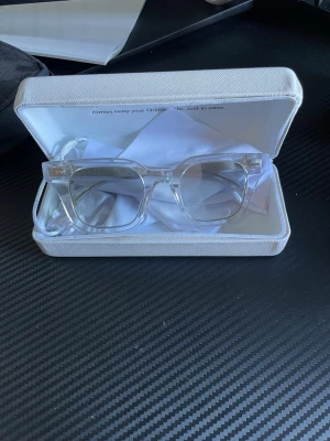 Transparenta glittriga solglasögon - Säljer ett par trendiga solglasögon med transparent båge och glittriga detaljer på skalmarna. Rektangulär form som ger en cool vibe och passar till många olika looks. Kommer med ett vitt fodral och putsduk.