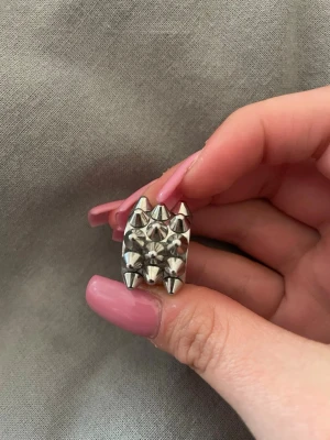 Silvrig ring med nitar och konformade detaljer - Cool och chunky ring i silverfärgad metall med flera konformade nitar på ovansidan. Ringen har en bred design och ger en edgy vibe, perfekt för dig som gillar statement-smycken. Passar till dig som vill sticka ut med din stil.