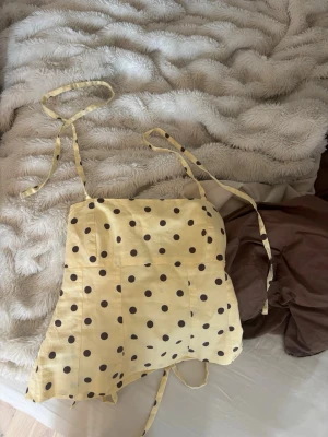 Gul prickig linnetopp  - Supersöt gul linnetopp från gina tricot med bruna prickar och tunna axelband som kan knytas. Toppen har en lätt utsvängd passform och är perfekt för varma dagar. Materialet känns lätt och luftigt, och mönstret ger en lekfull vibe. Säljer då den är för liten💕