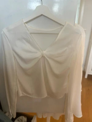 Vit långärmad blus med knut framtill - Säljer en stilren vit blus med lång ärm och snygg knutdetalj framtill. Blusen har en lätt transparent känsla och ett flowy fall, perfekt för dig som gillar en chic och enkel look.