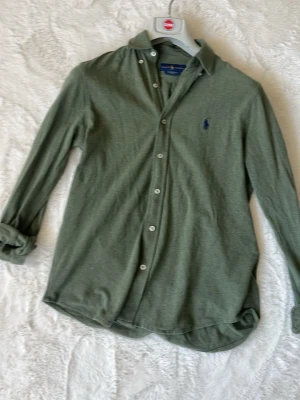 Ralph Lauren skjorta - Stilren grön skjorta från Ralph Lauren med klassisk krage och knappar framtill. Skjortan har lång ärm och den ikoniska broderade loggan på bröstet. Perfekt för en avslappnad men ändå snygg look. Passar mig som är 177 på bilden och väger 65kg