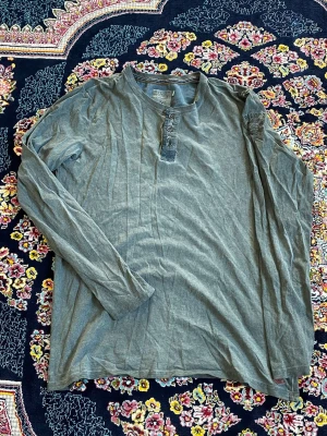Olivgrön långärmad topp med knappar - Snygg olivgrön långärmad topp med knappar framtill. Toppen har en enkel och avslappnad passform, perfekt att styla med jeans eller kjol. Tillverkad i mjukt bomullsmaterial för en bekväm känsla.