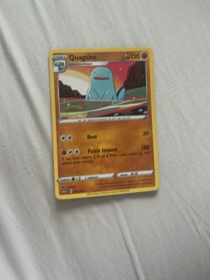 Pokémonkort Quagsire - Säljer ett Pokémonkort med Quagsire, en blå vatten- och marktyp Pokémon. Kortet har en gul ram och visar Quagsire i en tecknad landskapsmiljö. Kortet har attackerna Beat och Fickle Impact samt 120 HP. Perfekt för samlare eller Pokémon-fans.