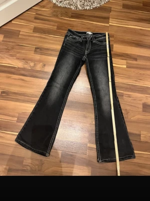 Svarta bootcut jeans med vita sömmar - Snygga svarta bootcut jeans med markerade vita sömmar och klassisk femficksmodell. Jeansen har låg midja och lätt utsvängda ben för en trendig siluett. Perfekta för dig som gillar en avslappnad men ändå stilren look.
