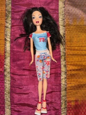 Barbie – brunett – vintage Y2K docka - Original My Scene Barbie från tidigt 2000-tal med klassisk Y2K-stil och ikonisk My Scene-look. Dockan har långt mörkt hår, markerad makeup och outfit med “My Scene 75”-topp, mönstrade capribyxor och matchande skor enligt bilderna.  Dockan är i mycket bra vintage-skick med fint ansikte, välbevarat hår och fina kläder. Perfekt för samlare, nostalgiker eller dig som älskar My Scene, Barbiecore och tidigt 2000-tal.  En eftertraktad docka från den populära My Scene-serien från Mattel. 