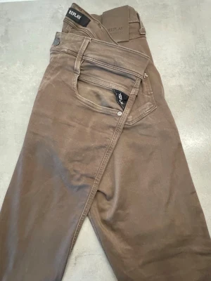 Bruna jeans från Replay - Snygga bruna jeans från Replay med klassisk femficksdesign och raka ben. Jeansen har en stilren look med diskreta sömmar och Replay-logga på etiketten i linningen. Perfekta för dig som gillar en enkel men trendig stil. Ny tvättade 