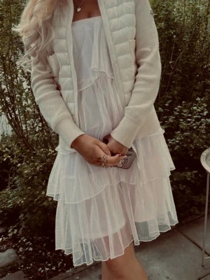 Vit volangklänning med axelbandslös design - Söt ljusrosa klänning med flera lager volanger och. Klänningen. perfekt för varma dagar. Materialet ser ut att vara lätt och skir, vilket ger en drömmig look.