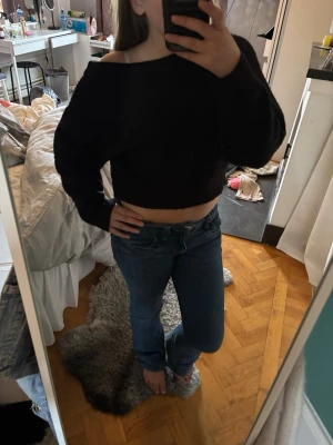 Svart croppad stickad topp - Svart croppad stickad topp med offshoulder-design och långa ärmar. Perfekt för en trendig och avslappnad stil. Mjuk och skön att bära.