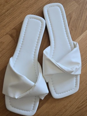 Vita sandaler  - Vita sandaler med twistade remmar i konstläder. Perfekta för en avslappnad look! Helt oanvända, de sitter lite för tajt på mig. Passar den som alltid har 37 i storlek eller den som har 36 ½. 