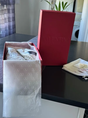 Valentino Garavani vita sneakers - Säljer ett par vita sneakers från Valentino Garavani med svart detalj över mitten. Skorna har klassisk låg profil, rund tå och är tillverkade i läder. Kommer med originalkartong och dustbag. Perfekta för dig som gillar exklusiv och stilren design.