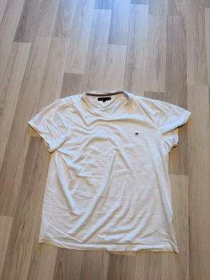 Vit t-shirt från Tommy Hilfiger - Klassisk vit t-shirt från Tommy Hilfiger med rund halsringning och liten broderad logga på bröstet. Tillverkad i mjuk bomull och har en normal passform. Perfekt basplagg för en enkel och stilren look.