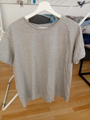 Grå basic t-shirt från Lager 157 - Enkel och stilren grå t-shirt från lager 157 i storlek XL. T-shirten är kortärmad och tillverkad i en mjuk blandning av bomull och viskos, perfekt för en avslappnad look. Passar dig som gillar minimalistisk stil.