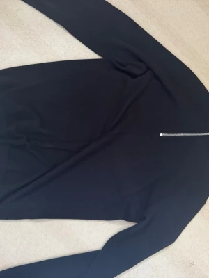 Svart stickad tröja med half zip - En svart stickad tröja med lång ärm och half zip-dragkedja vid halsen. Enkel och stilren design som passar till det mesta. Perfekt för dig som gillar klassiska plagg med en modern twist.