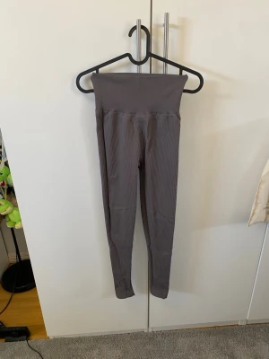 Grå ribbade seamless leggings - Säljer ett par grå leggings med ribbad struktur och hög midja. De är sömlösa och har en tight passform som formar sig efter kroppen. Materialet är stretchigt och mjukt, perfekt för både träning och chill. Inget synligt märke på plagget.