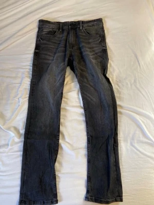 Svarta slim fit jeans - Snygga svarta slim fit jeans med klassisk femficksdesign och diskreta slitningar. Jeansen har normal midja och raka ben, perfekta för en stilren och avslappnad look. Passar till det mesta och är ett måste i garderoben.