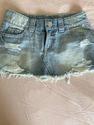 Ljusblå jeanskjol med slitningar ifrån Gina tricot 14+ - En kort ljusblå jeanskjol med slitna detaljer och fransig kant. Den har fem fickor, den är ifrån Gina tricot i storlek xxs.💓