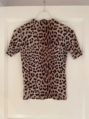 Leopardmönstrad topp med kort ärm - Snygg topp med leopardmönster i beige och bruna toner. Toppen är i tunt tyg men inte genomskinlig och stretchig. I mycket bra skick! Storlek XS