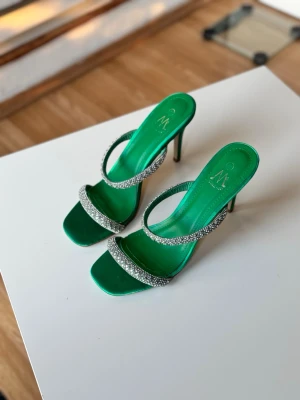 Gröna klackskor  - Snygga gröna pumps med två glittriga strassband och hög smal klack. Skorna har öppen tå och fyrkantig framdel, vilket ger en trendig look. Tillverkade i ett glansigt material som verkligen sticker ut. Perfekta för dig som vill ha något extra.