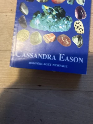 Kristallernas kraft av Cassandra Eason - En bok med blått omslag av Cassandra Eason, dekorerad med bilder på olika kristaller. Boken handlar om kristallers egenskaper och hur de kan användas för healing och personlig utveckling. Perfekt för dig som är nyfiken på kristaller och deras betydelse.