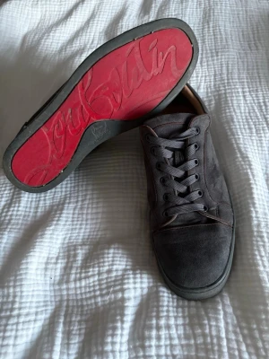 Gråa Louboutin - Säljer ett par gråa sneakers från Christian Louboutin med klassisk röd sula och ovandel i mjuk mocka. Skorna har gråa skosnören, diskreta sömmar och en låg silhuett. Perfekta för dig som vill ha en stilren och lyxig sneaker med ikonisk design. Ingen box finns tyvärr, kontakta vid minsta fundering!