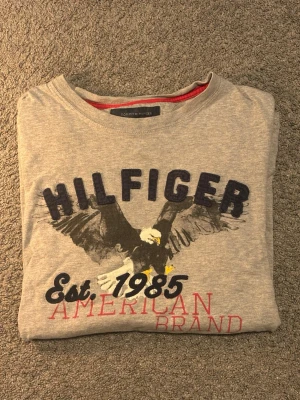 Grå Hilfiger t-shirt med örntryck - Grå t shirt från Tommy Hilfiger, mycket bra skick, storlek M, 100% bomull.