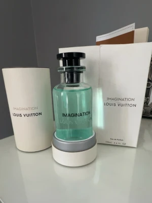 Louis Vuitton Imagination parfym 100ml - Lyxig parfym från Louis Vuitton, Imagination, i en stilren glasflaska med turkosblå vätska och svart lock med LV-logga. Kommer i exklusiv vit förpackning med silverdetaljer. Flaskan rymmer 100 ml Eau de Parfum.
