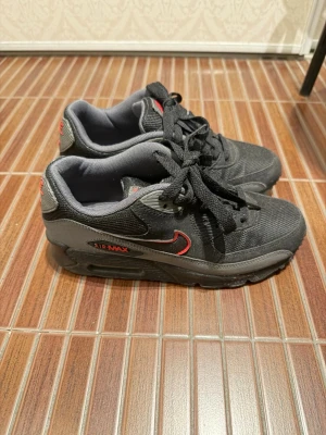 Nike Air Max svarta sneakers 36,5 - Snygga svarta Nike Air Max sneakers med röda detaljer och klassisk swoosh på sidan. Skorna har en låg silhuett, mesh och syntetmaterial samt tydlig Air Max-dämpning i sulan. Perfekta för dig som gillar streetwear och sportig stil.