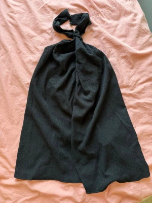 Svart halterneck topp från Pull&Bear - Snygg svart halterneck topp med knäppning i nacken. Toppens tyg har en lätt struktur och faller fint. Perfekt för dig som gillar en stilren och trendig look. Använd en gång!