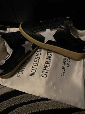 Golden Goose Ball Star sneakers  - Snygga Golden Goose Ball Star sneakers i svart skinn med vit stjärna på sidan. De har mörkblå snörning men tillkommer en svart eller vit snöre med på köpet. (Se sista bild). Perfekt för dig som gillar stil. Storlek 40 