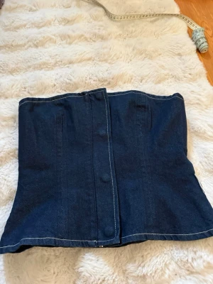 Mörkblå denim korsettopp - Trendig mörkblå korsettopp i denim med markerade sömmar och lätt utsvängd form. Toppen är axelbandslös och passar till både jeans och kjol. Stängs med knapp och har en snygg, strukturerad passform. Köpt på Sellpy men och i nyskick, ej använd mer än provat. Obs! En knapp är lite trasig men märks inte💗💗💗