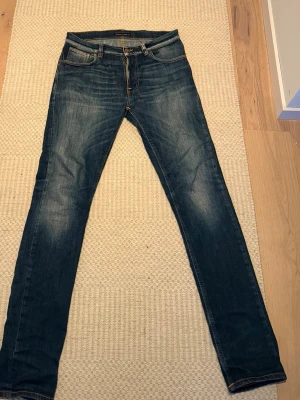 Blå slim fit jeans från Nudie Jeans - Snygga blå slim fit jeans från Nudie Jeans med klassisk femficksdesign och orangea sömmar. Jeansen har en lätt tvättad look och smala ben. Perfekta för dig som gillar en stilren och modern look.