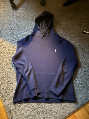 Marinblå hoodie från Polo Ralph Lauren - Snygg marinblå hoodie från Polo Ralph Lauren med klassisk broderad logga på bröstet. Tillverkad i ett strukturerat, lite tjockare material och har en stor känguruficka framtill samt huva med dragsko. Perfekt för en chill och stilren look. Pris kan självklart diskuteras!