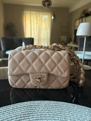 Beige/ rosa väska  - Superfin quiltad mini bag i ljusrosa med guldfärgade detaljer och kedjerem. Väldigt elegant och passar både vardag och fest Bra skick och knappt använd. Rymmer mobil, kort, nycklar och små essentials. Sälj pga att den ej används och är öppen för bud!! 