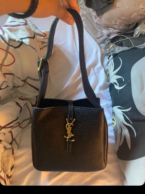  handväska i läder - Snygg svart handväska från i  läder framtill. Väskan har en justerbar axelrem med gulddetalj och en stilren, fyrkantig form. Perfekt för dig som vill ha en klassisk och trendig accessoar. Den är använd och har några så defekter på. 