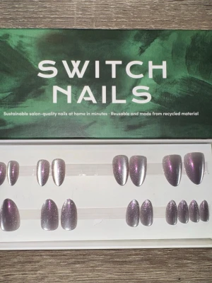 Switch Nails Violet Cat Eye Almond - Press-on naglar från Switch Nails i färgen Violet Cat Eye. Naglarna har en glittrig, violett finish och är i kort almondform. Tillverkade av återvunnet material och kan återanvändas. Perfekt för dig som vill ha snygga naglar snabbt och enkelt.