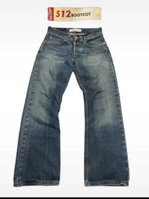Levi's 512 Bootcut jeans blå denim - Klassiska Levi's 512 Bootcut jeans i blå denim med snyggt slitna detaljer. Modellen har bootcut-passform med utsvängda ben och fem fickor. Perfekta för en avslappnad och trendig look. Tillverkade i bomull.