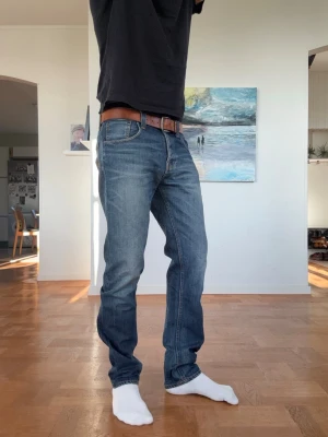 Blå jeans från Nudie Jeans - Jag på bilden är 189cm\ 85kg . Modellen heter steady Eddie och är en straight fit.                                                                    Snygga blå jeans från Nudie Jeans med klassisk femficksdesign och raka ben. Jeansen har en lätt tvättad look och kontrastsömmar, samt detaljerade bakfickor med Nudie Jeans signatursöm. Perfekta för en avslappnad stil.