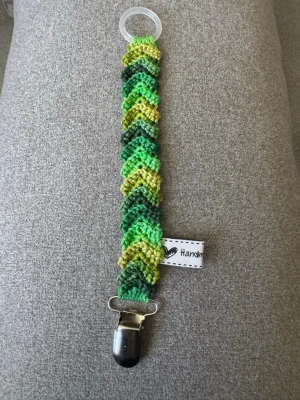 Virkad napphållare - Virkad napphållare i gröna nyanser. Virkad av mig i 100% bomullsgarn med metallclip och silikonring.  Mönsterskapare: animo.design