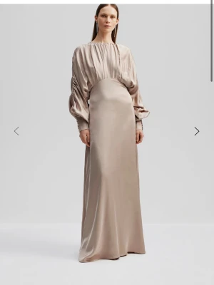 Lång champagnefärgad satinklänning - En Malina långklänning i champagnefärgad satin med draperad överdel och vida långärmar. Klänningen har en markerad midja och ett mjukt, flytande fall. Säljs inte längre på Malinas hemsida🩷storlek 36 men passar 38!! Nypris: 4600kr 