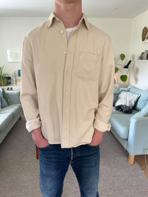 Beige Skjorta/Overshirt - Stilren beige skjorta i mjuk bomull med klassisk krage och bröstficka. Skjortan har långa ärmar och knäppning framtill. Perfekt för en avslappnad men snygg look.