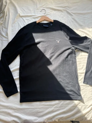 Svart långärmad topp från Gant Storlek S - Helt oändvänd! Svart långärmad topp från Gant i mjuk bomull. Klassisk rund halsringning och diskret Gant-logga broderad på bröstet. Perfekt för en clean och stilren look.
