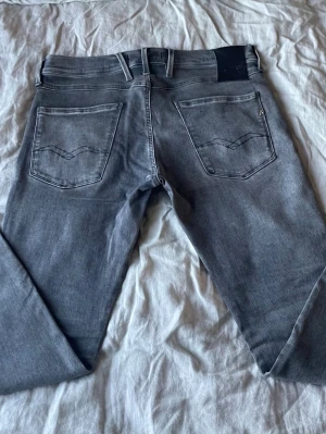 Replay Jeans Hyperflex - Snygga grå jeans från Replay, modell Anbass Hyperflex. Klassisk femficksdesign med raka ben och detaljerade bakfickor. Jeansen har en diskret tvättad look och är tillverkade i mjukt denimtyg för skön passform. Perfekta för en avslappnad och trendig stil.