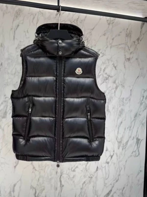 Svart dunväst från Moncler - Snygg svart dunväst från Moncler med glansig finish, vadderad design och avtagbar huva. Västen har två dragkedjeförsedda fickor fram och Moncler-logga på bröstet. Perfekt för lager-på-lager och streetstyle.