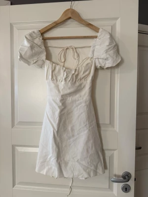 Vit kortklänning med puffärm - Supersöt vit kortklänning med puffiga kortärmar och snörning i ryggen. Säljer då den inte komemr till användning! Skicka om ni undrar något 💕💕