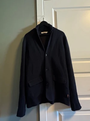 Mörkblå kavaj/ Overshirt - Stilren mörkblå kavaj med tre knappar framtill och två fickor med lock. Klassisk passform och mjukt material som ger en avslappnad men ändå dressad look. Perfekt för dig som vill ha en enkel men snygg kavaj till garderoben.